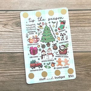 May include: A rectangular Christmas-themed card with a light blue plaid background and gold circles. The card features illustrations of Christmas lights, a tree, stockings, candy canes, and a truck. Text includes "tis the season" and "stuff and budget".