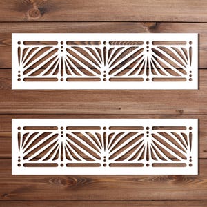 May include: Two white decorative stencils with a repeating geometric design. Each stencil features a series of rectangular panels with a fan-like pattern and dotted accents. The stencils are placed on a wooden surface.