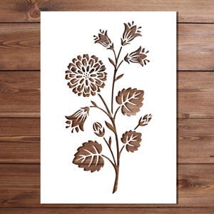 May include: A wooden floral stencil featuring a detailed flower and leaf design. The stencil is cut from a dark brown wood, with intricate details of the flower petals and leaf veins. The design is set against a white background.