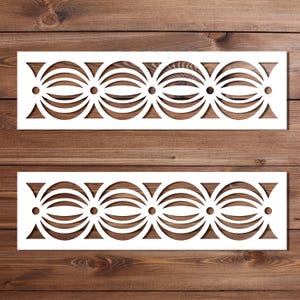May include: Two white, rectangular stencils with a repeating geometric design of connected circles and curved lines. The stencils are placed on a dark brown wooden surface, creating a contrast between the white design and the wood grain.