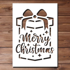 Puede incluir: Diseño de corte de papel blanco de una caja de regalo con un lazo y el texto "Feliz Navidad".