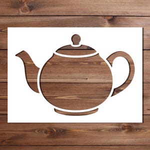 May include: A white stencil featuring a cutout silhouette of a classic teapot with a rounded body, a curved handle, a spout, and a lid with a small knob. The design is presented as a flat, die-cut template with clean, bold outlines.