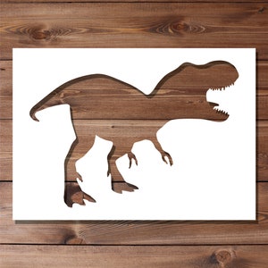 May include: White silhouette of a dinosaur, a Tyrannosaurus Rex, cut out of a white sheet of paper. The dinosaur is facing right and has its mouth open. The silhouette is set against a brown wood background.