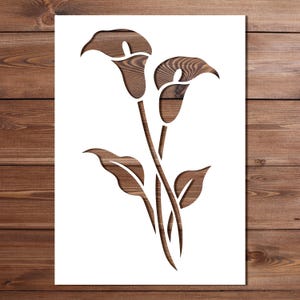 May include: A wooden cutout of calla lilies with stems and leaves. The flowers and leaves are a medium brown color, and the background is white. The cutout is placed on a wooden surface.