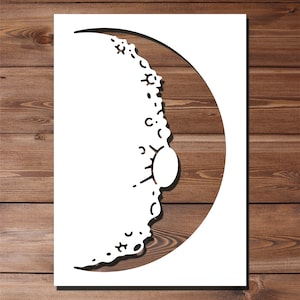 May include: White paper cut-out of a crescent moon with a decorative design around the edge. The moon has a small circle cut out in the center.