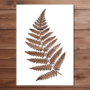 May include: A brown wooden fern leaf design on a white background. The fern is a detailed cutout, showcasing the wood grain. The artwork is set against a backdrop of wooden planks, creating a natural aesthetic.