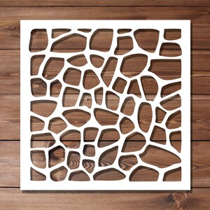 Puede incluir: Plantilla blanca con un patrón geométrico de círculos superpuestos, que recuerda a una pared de piedra o un panal de abejas. La plantilla está sobre un fondo de madera marrón.