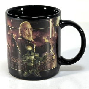 May include: Black ceramic mug featuring a movie scene with a character in a dark outfit. The mug has a black handle and interior. The background of the scene is a fiery red and orange color.