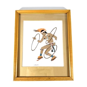 May include: Framed artwork featuring a Native American dancer with two hoops. The dancer is depicted in motion, wearing traditional attire with orange, brown, and blue accents. The artwork is set in a gold-colored frame.