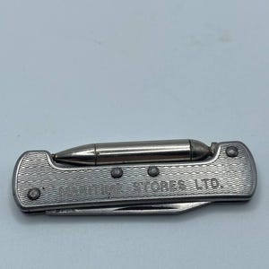 May include: A silver-toned metal pocket knife featuring a textured wavy pattern on the handle and the text MARITIME STORES LTD. embossed on the side. A small, cylindrical metal tool is attached to the top edge of the handle, and a blade is visible.