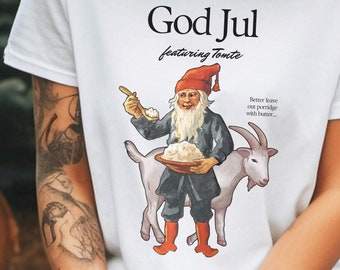 May include: White t-shirt featuring a graphic of a gnome holding a bowl of porridge and a goat. The text "God Jul featuring Tomte" is printed above the graphic. The text "Better leave out porridge with butter..." is printed to the right of the graphic. The text "arriving December 24 (but never through the chimney)" is printed below the graphic.