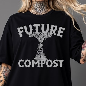 May include: Black t-shirt with the words "FUTURE COMPOST" in a distressed, gray font. The design features a stylized graphic between the words. The shirt has short sleeves and a relaxed fit.