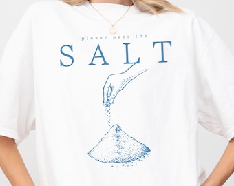 May include: White t-shirt with a blue graphic of a hand pouring salt onto a pile of salt. The text "please pass the SALT" is printed above the graphic.