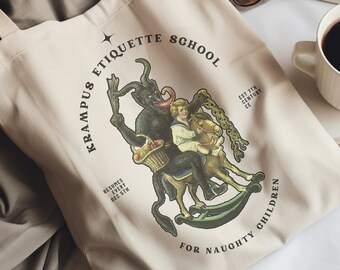 May include: A beige canvas tote bag featuring a black and white illustration of a devil figure holding a child on a rocking horse. The text on the bag reads "Krampus Etiquette School Est 17th Century CE Lessons Every Dec 5th For Naughty Children".