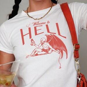 May include: White t-shirt with a red graphic of a devil with the text "Welcome to HELL" printed on it.