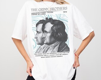 Może przedstawiać: Biała koszulka z grafiką braci Grimm, tekstem "THE GRIMM BROTHERS" i "GRIMM'S FAIRY TALES: HANS IN LUCK 1812". Zawiera również cytat. Koszulka ma krótkie rękawy.