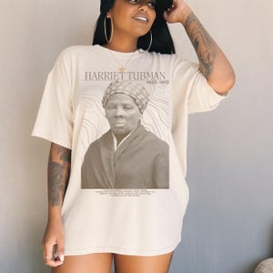May include: A beige t-shirt with a black and white image of Harriet Tubman. The text "Harriet Tubman 1822-1913" is printed above the image. A quote from Harriet Tubman is printed below the image: "I had reasoned this out in my mind, there was one of two things I had a right to, liberty or death; if I could not have one, I would have the other."