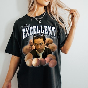 Puede incluir: Camiseta negra con la frase "What Excellent Boiled Potatoes" en blanco y azul. El diseño incluye una imagen de un hombre y varias patatas. La camiseta es de color oscuro.