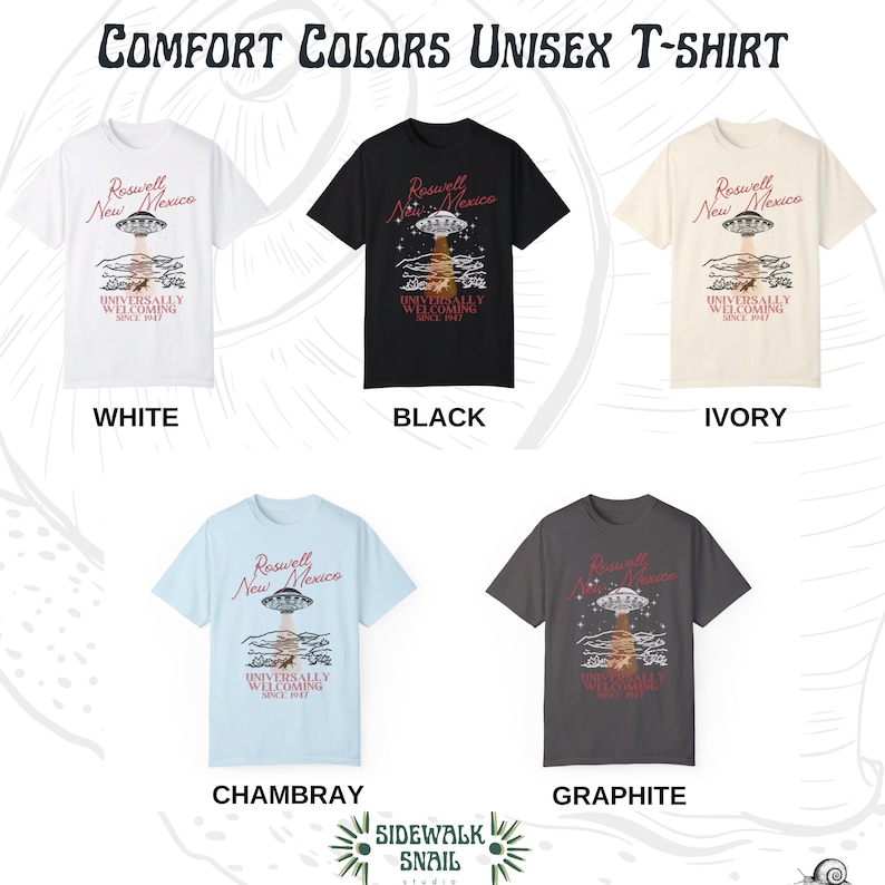 Puede incluir: Una camiseta unisex con un gr&aacute;fico de un OVNI sobre Roswell, Nuevo M&eacute;xico. El texto "Roswell New Mexico Universally Welcoming Since 1947" est&aacute; impreso en la camiseta. La camiseta est&aacute; disponible en seis colores: blanco, negro, marfil, chambray, grafito y gris jaspeado.