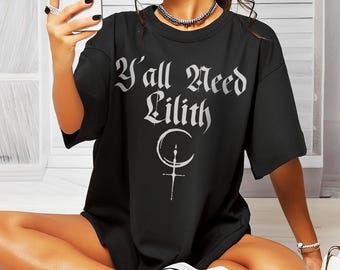 Puede incluir: Camiseta negra de gran tamaño con el texto "Y'all Need Lilith" en letras blancas y un símbolo de luna creciente y cruz plateado.