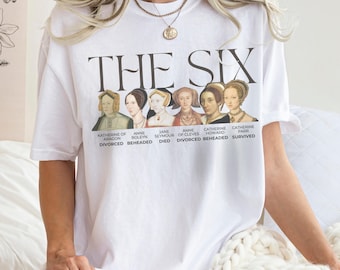 May include: White t-shirt with the text "THE SIX" and portraits of six women. The women are Katherine of Aragon, Anne Boleyn, Jane Seymour, Anne of Cleves, Catherine Howard, and Catherine Parr, with their fates below.