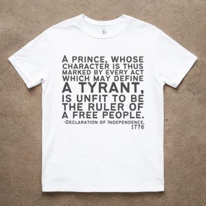 Puede incluir: Camiseta blanca con una impresión negra que dice "A Prince, Whose Character is Thus Marked by Every Act Which May Define A Tyrant, Is Unfit to Be the Ruler of a Free People. -Declaration of Independence, 1776"
