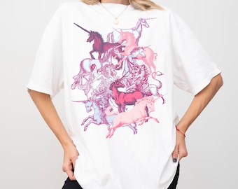 May include: White t-shirt featuring a colorful illustration of several unicorns in shades of pink, purple, and blue. The graphic design is centered on the front of the shirt. The shirt has short sleeves and a crew neck.