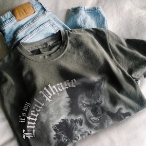 Peut inclure: Un t-shirt gris fonc&eacute; avec un imprim&eacute; graphique de deux loups hurlant &agrave; la lune. Le texte "It's my Full Moon Phase" est imprim&eacute; sur le t-shirt.