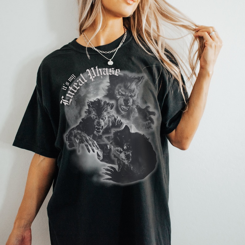 Peut inclure: T-shirt noir avec un imprim&eacute; graphique de trois loups-garous dans diff&eacute;rentes phases de transformation. Le texte "It's my Lyrical Phase" est imprim&eacute; sur le t-shirt.