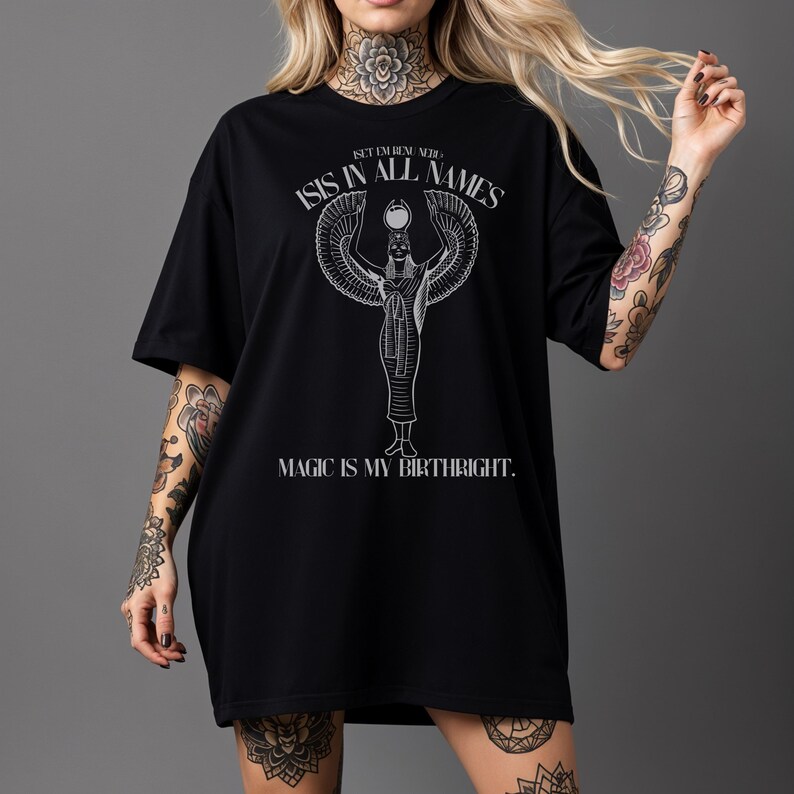 May include: Black t-shirt featuring a white graphic of an Egyptian deity with outstretched wings, the text "ISIS IN ALL NAMES" and "MAGIC IS MY BIRTHRIGHT." The shirt has a relaxed fit.