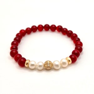 May include: A red and white beaded bracelet with a gold accent bead. The bracelet is made with small, round beads and has a simple design.