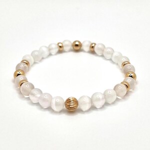 May include: White gemstone bracelet with gold beads and a gold accent bead. The bracelet is made of round beads and has a simple design.