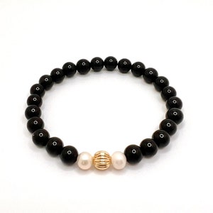 May include: Black beaded bracelet with two white beads and a gold bead in the center.