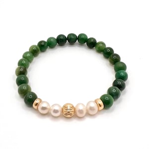 May include: A beaded bracelet featuring dark green round stones interspersed with white pearls and gold-colored accents. The bracelet is strung on an elastic band, creating a flexible and comfortable fit. The bracelet is a stylish accessory.