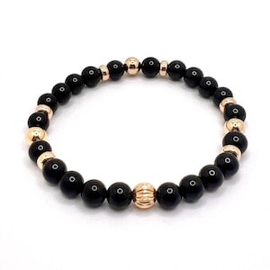 Puede incluir: Pulsera de cuentas de ónix negro y oro rosa. La pulsera tiene una sola cuenta de oro rosa más grande en el centro.