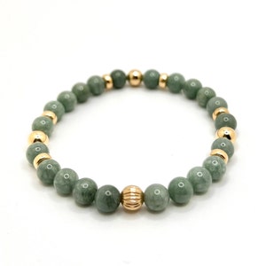 May include: A green jade and gold bead bracelet. The bracelet is made with round green jade beads and gold spacer beads. The bracelet has a gold bead with a textured design in the center.