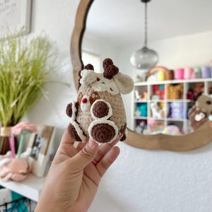 May include: A crocheted reindeer ornament made with brown and white yarn. The reindeer has a brown nose and brown eyes. The ornament is decorated with white and red sprinkles.