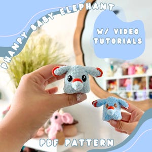 May include: A PDF pattern for crocheting a baby elephant plushie. The pattern includes video tutorials. The image shows two finished plushies, one blue and one pink, being held by a person's hands.