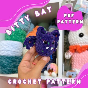 May include: A handmade, purple crochet bat with black eyes and white fangs. The bat has speckled details in various colors. Text on the image reads "BITTY BAT" and "CROCHET PATTERN". A pink graphic with the text "PDF PATTERN" is also visible.