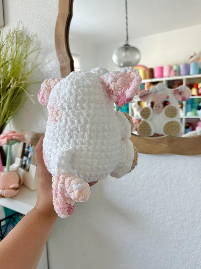 May include: A white crocheted sheep plush toy with pink accents. The sheep is holding a pink flower in its mouth.