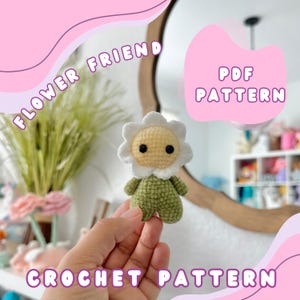以下が含まれることがあります： 花柄の友達のアミグルミの編み図。パターンはPDFでダウンロードできます。アミグルミは緑と白で、花の形をした頭をしています。