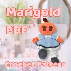 Può includere: Bambola Marigold all'uncinetto con testa arancione, occhi marroni e vestito blu. La bambola ha scaldamuscoli bianchi e grigi e una palla grigia. Il testo "Marigold PDF Crochet Pattern" è visualizzato in rosa.