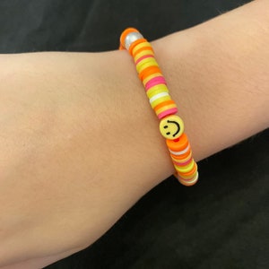 May include: A yellow, orange, and pink beaded bracelet with a silver bead and a smiley face charm.