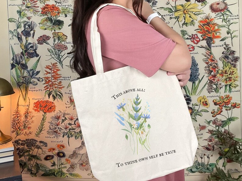 Pode incluir: Uma bolsa tote de lona branca com um design floral e o texto "This above all: To thine own self be true".