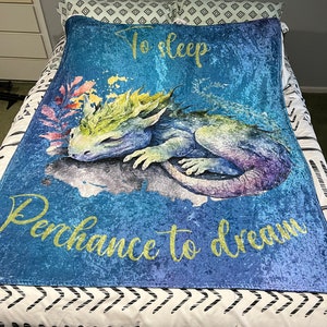 May include: A blue fleece blanket with a watercolor illustration of a sleeping dragon and the text "To sleep perchance to dream".