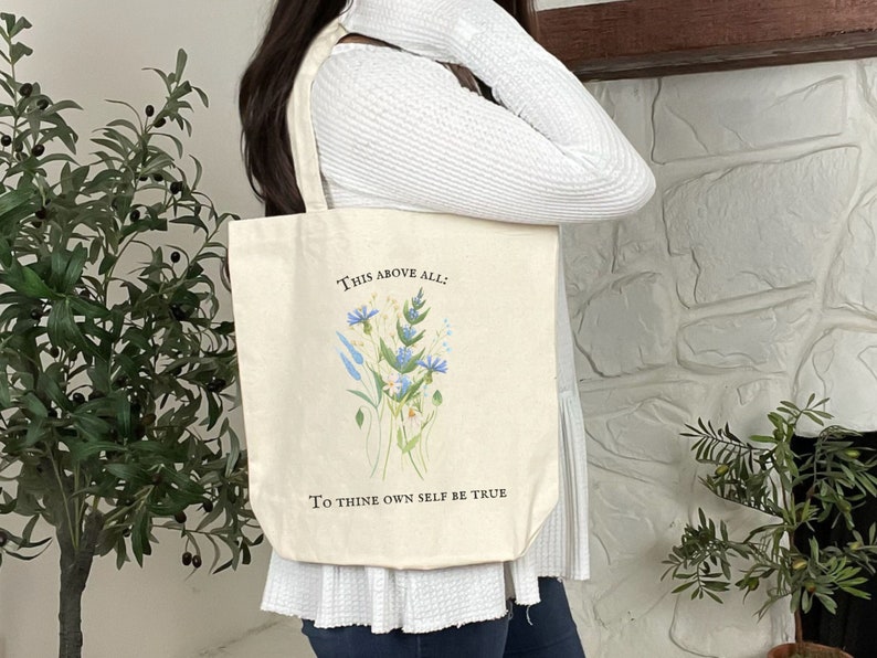 Pode incluir: Uma bolsa tote de lona branca com um design floral e o texto "This above all: To thine own self be true".