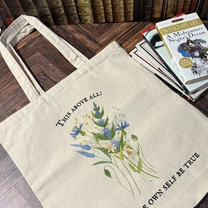 Pode incluir: Uma bolsa tote de lona bege com um design floral e o texto "THIS ABOVE ALL: TO THINE OWN SELF BE TRUE".