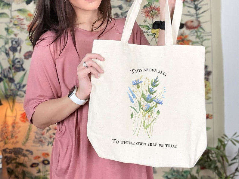 Pode incluir: Uma bolsa tote de lona branca com um design floral e o texto "This above all: To thine own self be true".