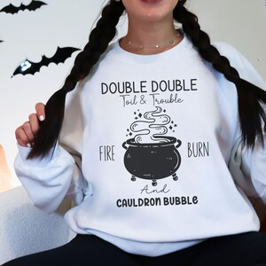 May include: White sweatshirt with a black and white graphic of a cauldron with smoke and the text "Double Double Toil & Trouble Fire Burn And Cauldron Bubble".