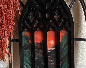 May include: Black framed wall art with a gothic arch design. The artwork features a sunset scene with a castle, a large sun, and green foliage. The frame is black and has cut-out details.